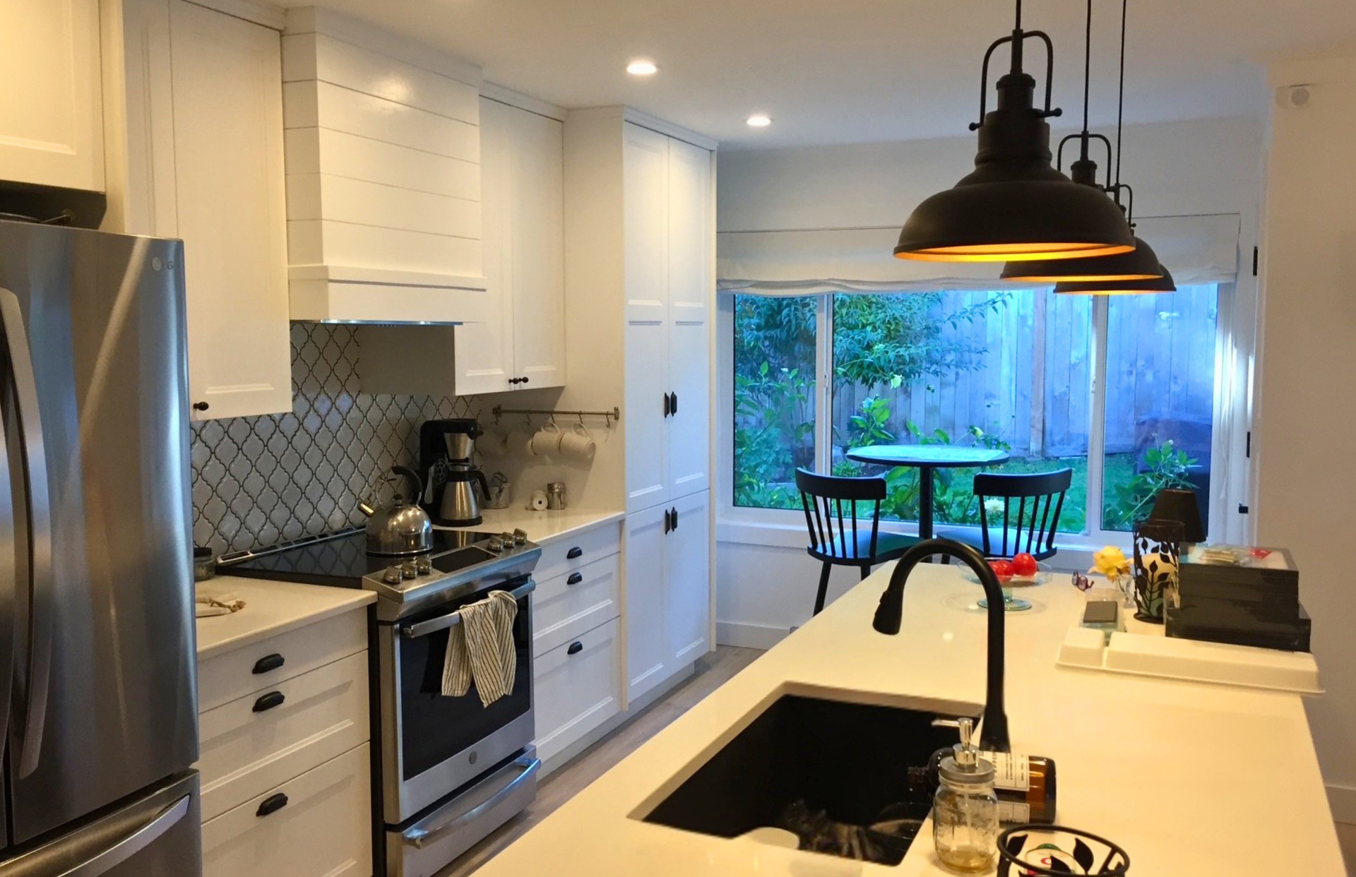 White shaker galley kitchen with shiplap range hood, pale-blue arabesque tile backsplash and black industrial pendants