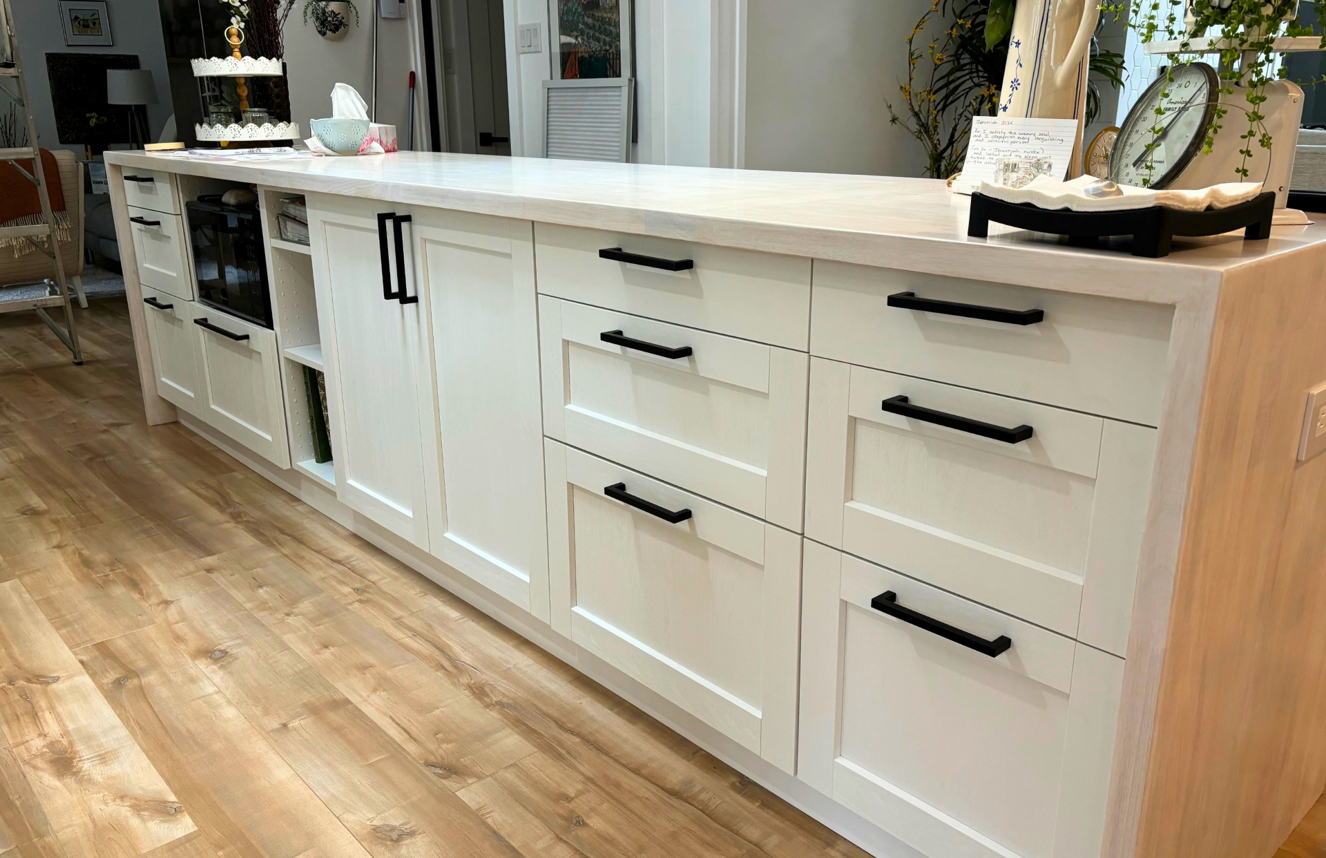 Long whitewashed shaker island with a light butcher-block-style top, matte-black bar pulls and wide-plank oak floors